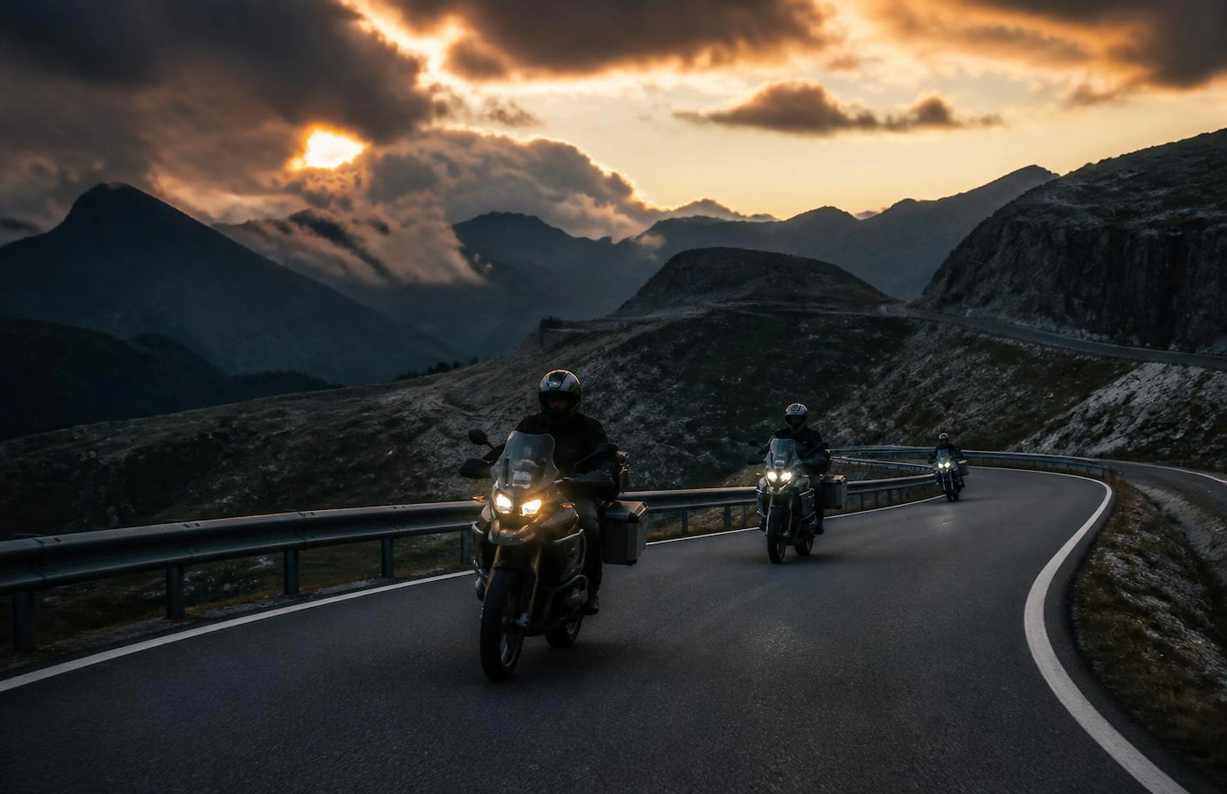 Group of adventure motorcycles riding a mountain switchback at golden hour